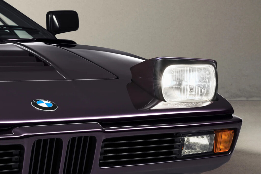 Techno Violet BMW M1 E26 by Ronnie Fieg & KITH closeup shot of the pop up headlight and BMW badge with the beige wall in the background and off white concrete floor.