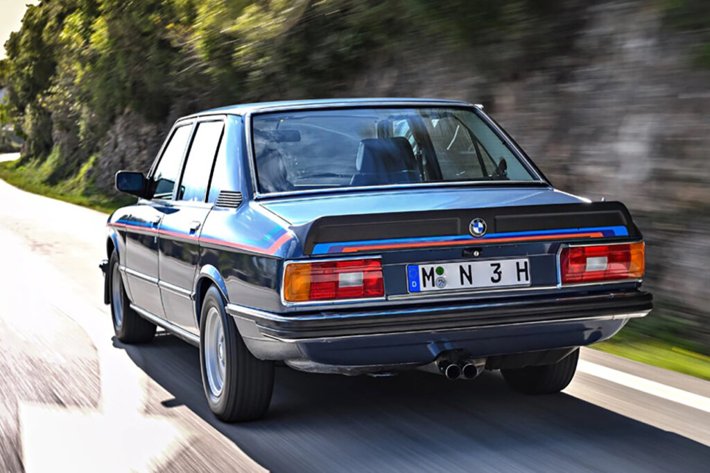 Blue M Division car the E12 M535i with M division stripe on the trunk and on the quarter panel with the car driving on a mountain road.