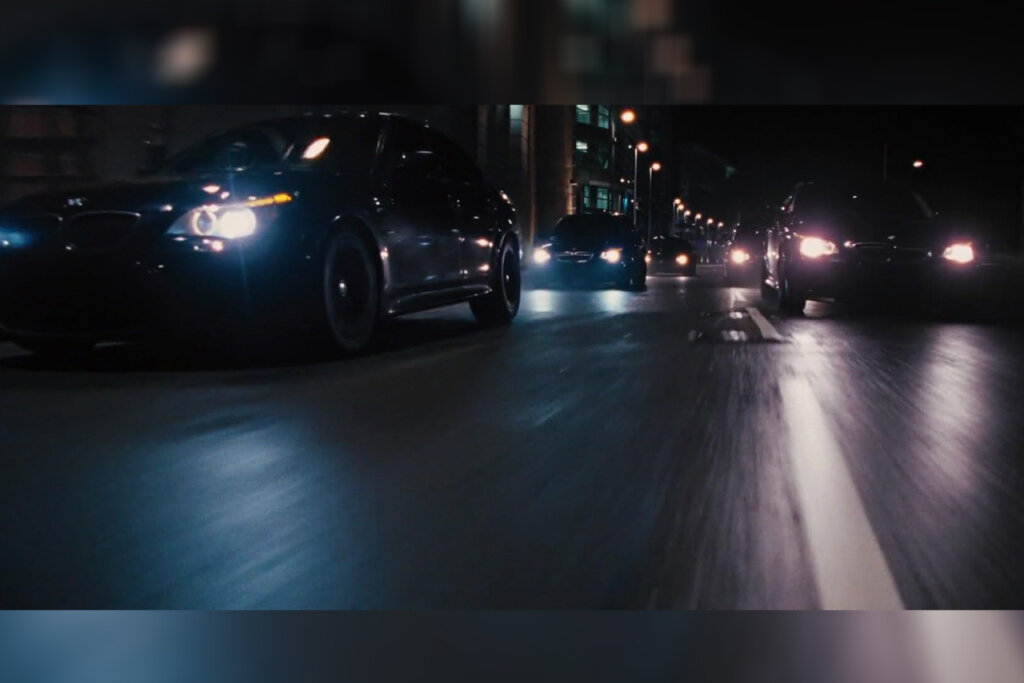 Black BMW M5 E60's with headlights on driving fast on a street in the film Fast and Furious 6.