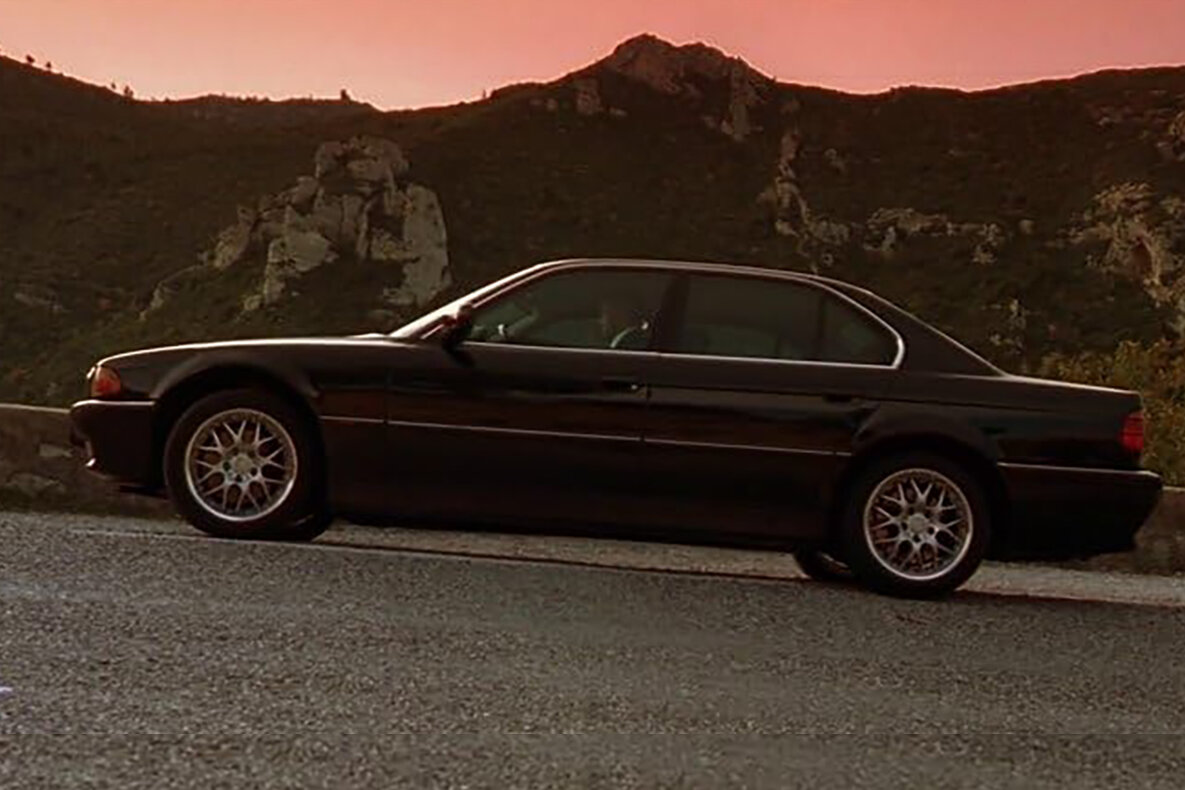 Black BMW 735i E38 saloon model side profile, with sun set red sky in the background.