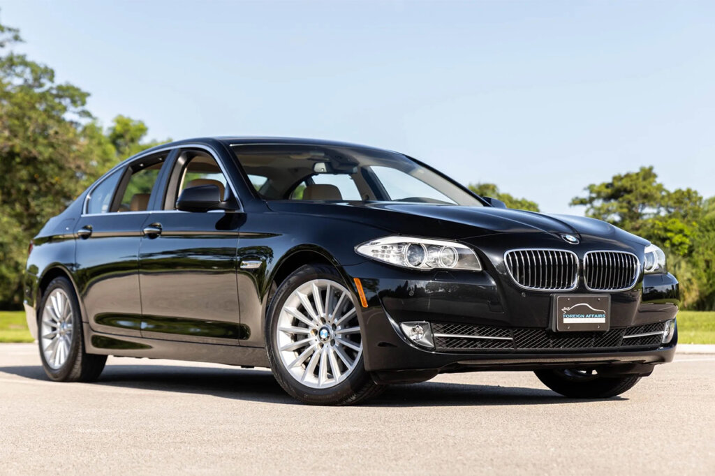 Black Saloon BMW F10 car with silver wheels parked at an angle with trees and blue sky in the background.