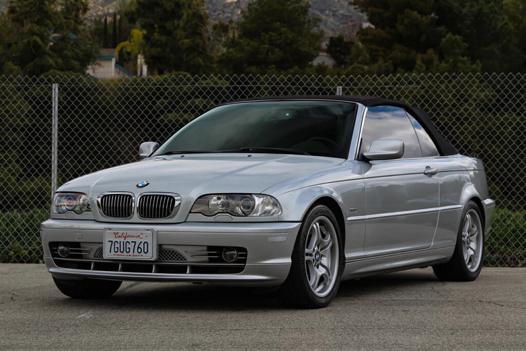 Silver BMW E46 Cabrio trim parked at an angle in front of bushes and trees on an asphalt road.