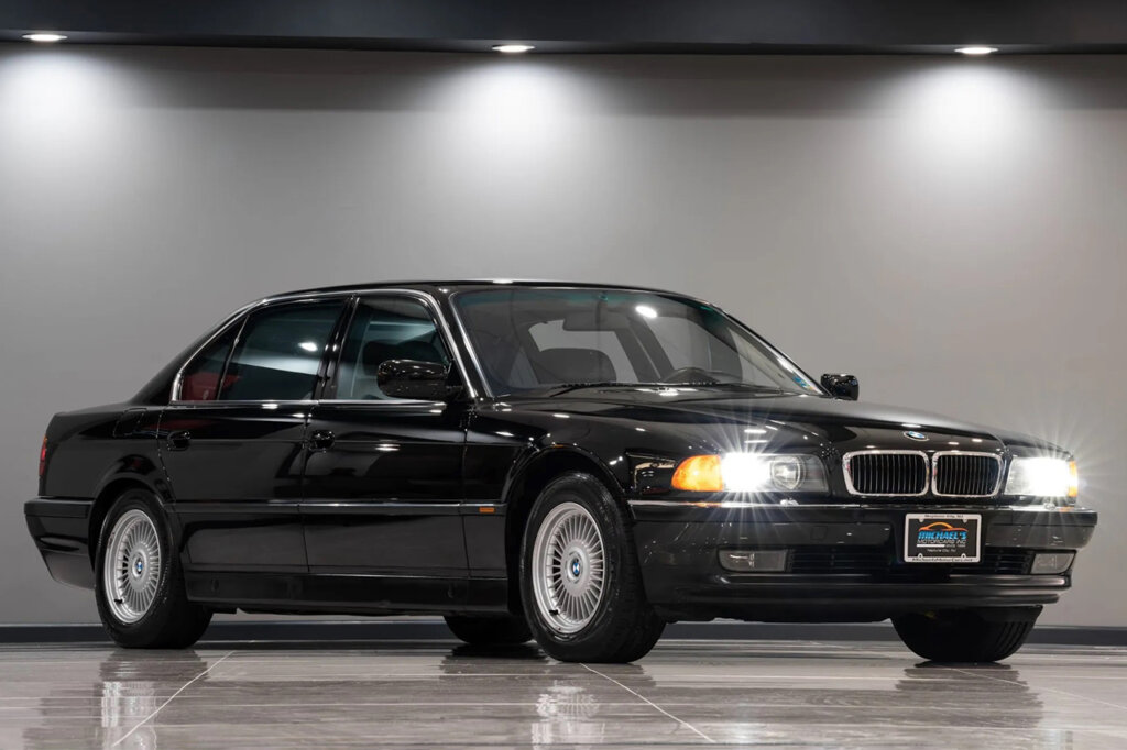 Black BMW 735i sedan with headlights on parked inside of a showroom floor with lights on above the car.