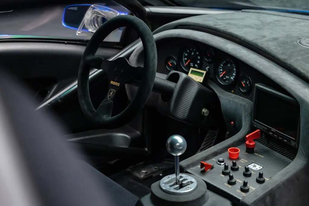 Modified racing interior with a Suede MOMO steering wheel with gated shifter and buttons and switches of a Lamborghini Diablo GTR.