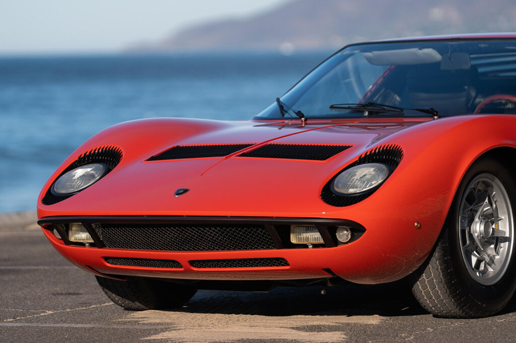 Red Lamborghini Miura P400 closeup of front end with two circular headlights above thin black grill.