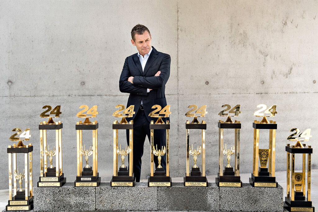 Man in a suit looking at his 9 trophies from the 24 hours of Le Mans endurance race.