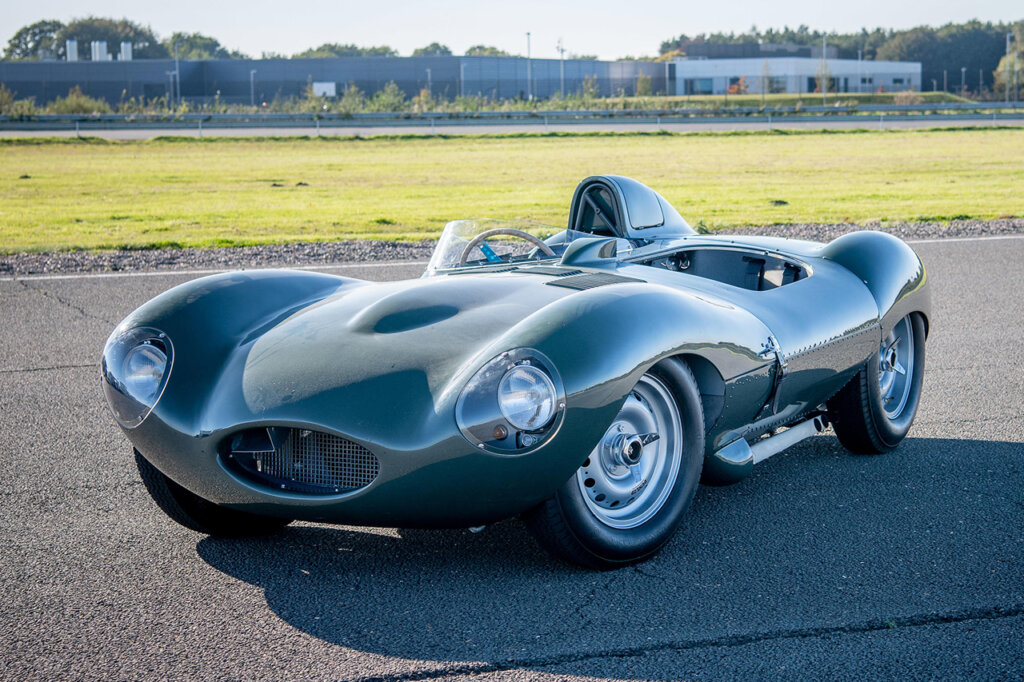 Restored green Jaguar D-Type parked at an angle on a race track with grass behind it.