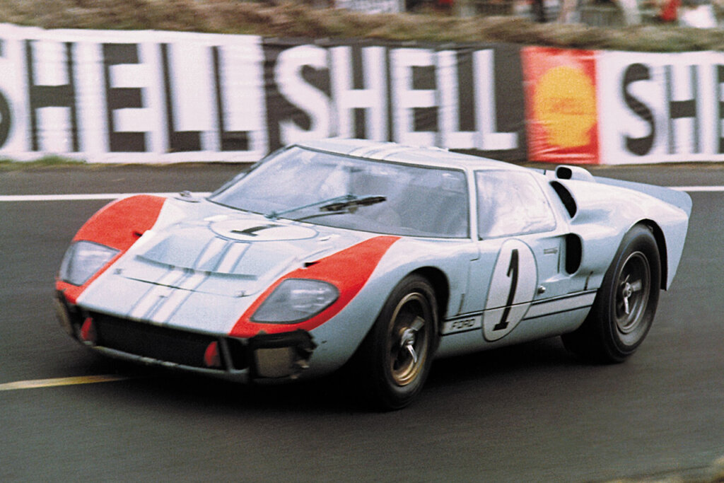 Color photo of a Ford GT40 with the number 1 on the door driving past banners saying Shell on it.