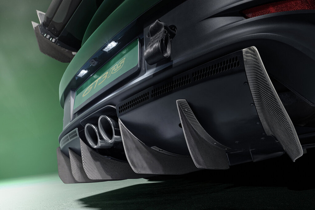 Closeup of rear carbon diffuser of a green Porsche 911 GT3 RS with a green wall in the background.