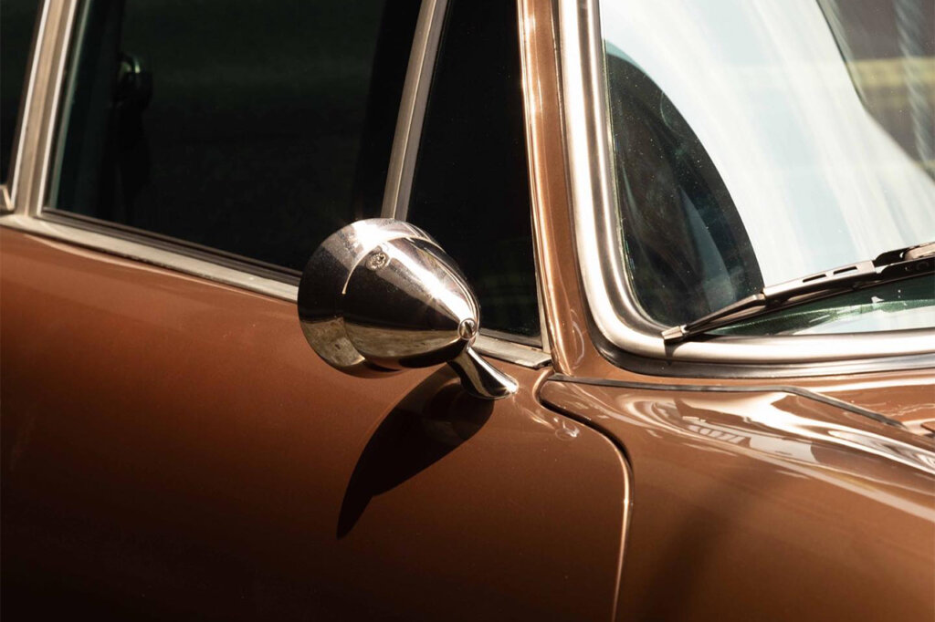 Brown Porsche 911 detail of a side mirror with a window glare on the front windshield.