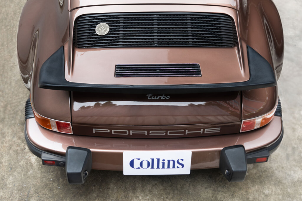 Porsche 911 rear end with a white license plate and the word Collins in blue on it.