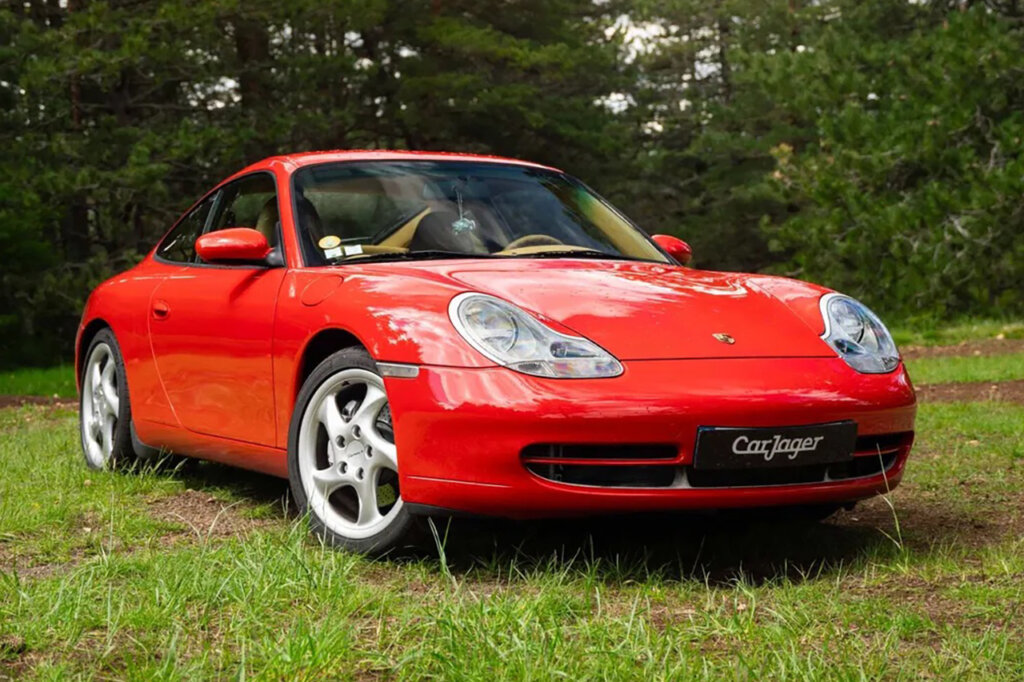 Red Porsche 996 carrera parked on the grass with trees in the background