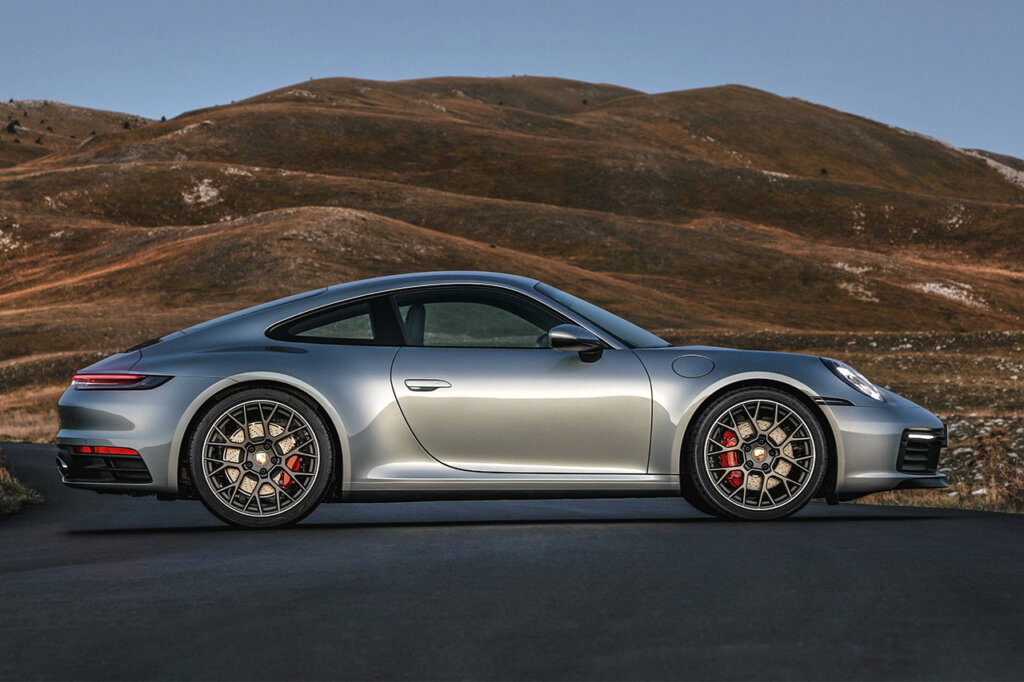 Silver Porsche 911 992 parked sideways on a road with brown mountains in the background