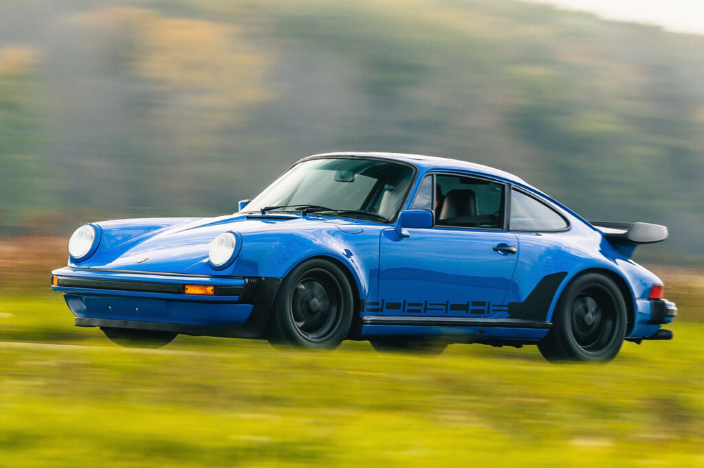 Blue Porsche 930 Carrera driving fast on a road with grass in the foreground