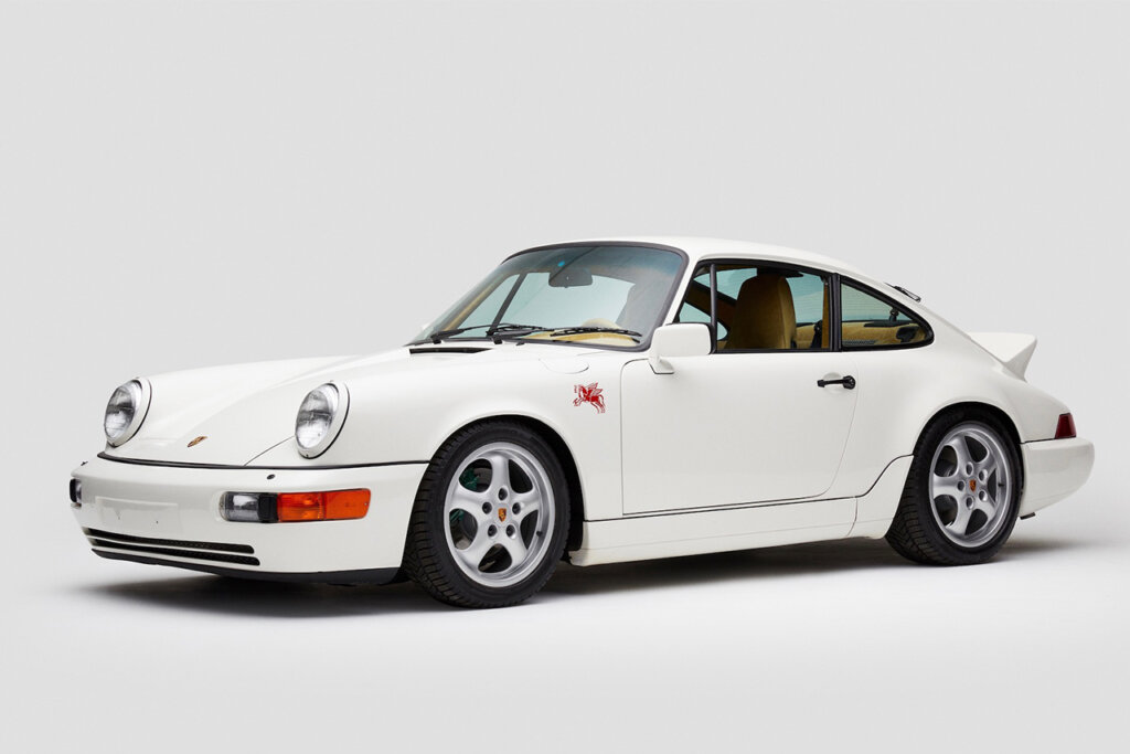 White 911 964 with a red icon on the fender parked in an all white room