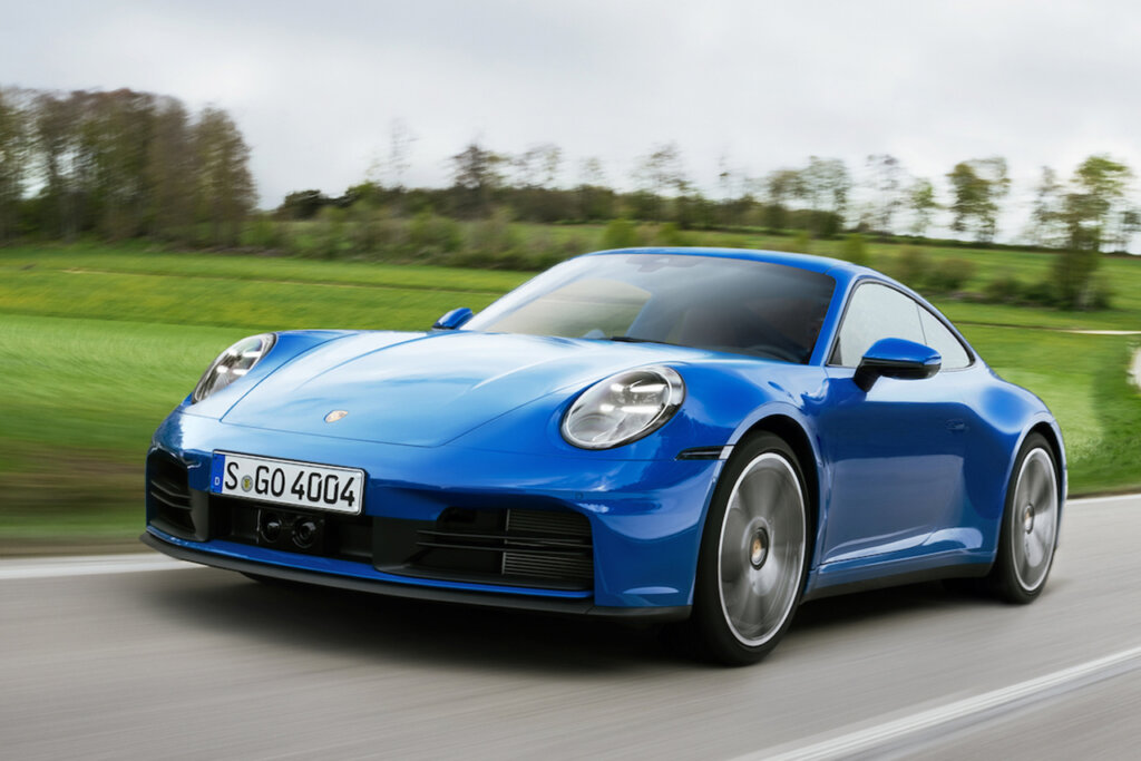 Blue 911 992 driving on a road fast passing a grassy field with trees