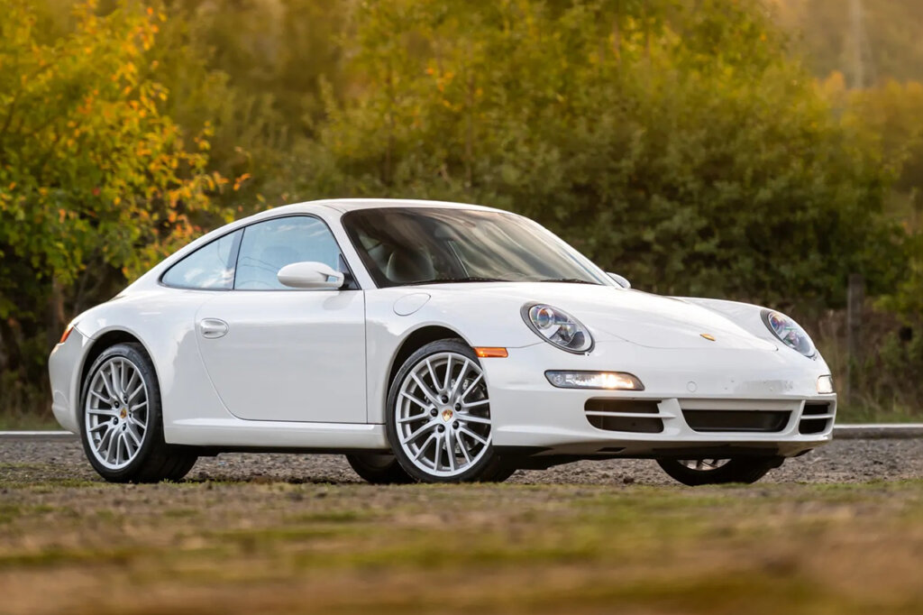 White Porsche 997 carrera parked with greenish yellow trees and grass in background and foreground