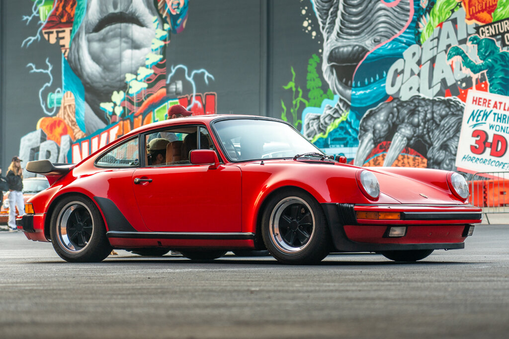 Red and black Porsche 911 930 carrera parked in front of a mural with colorful iconic monsters
