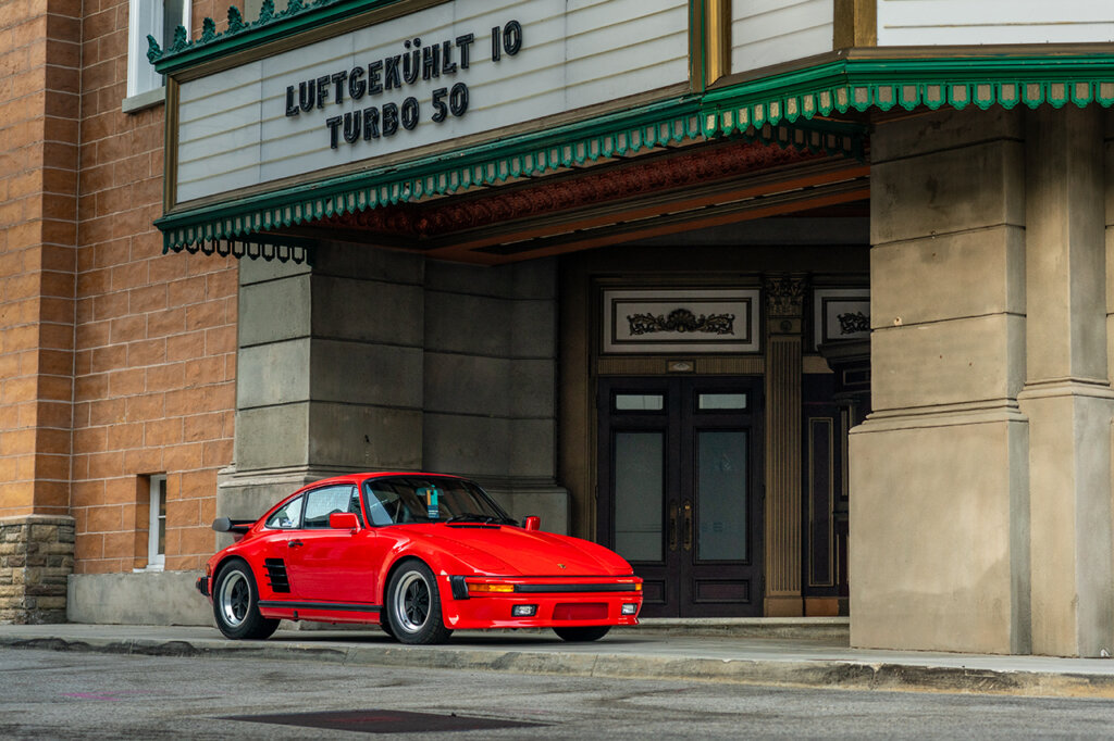 Porsche 930 slantnose parked in front of a theater with words Luftgekuhlt 10 Turbo 50 above it