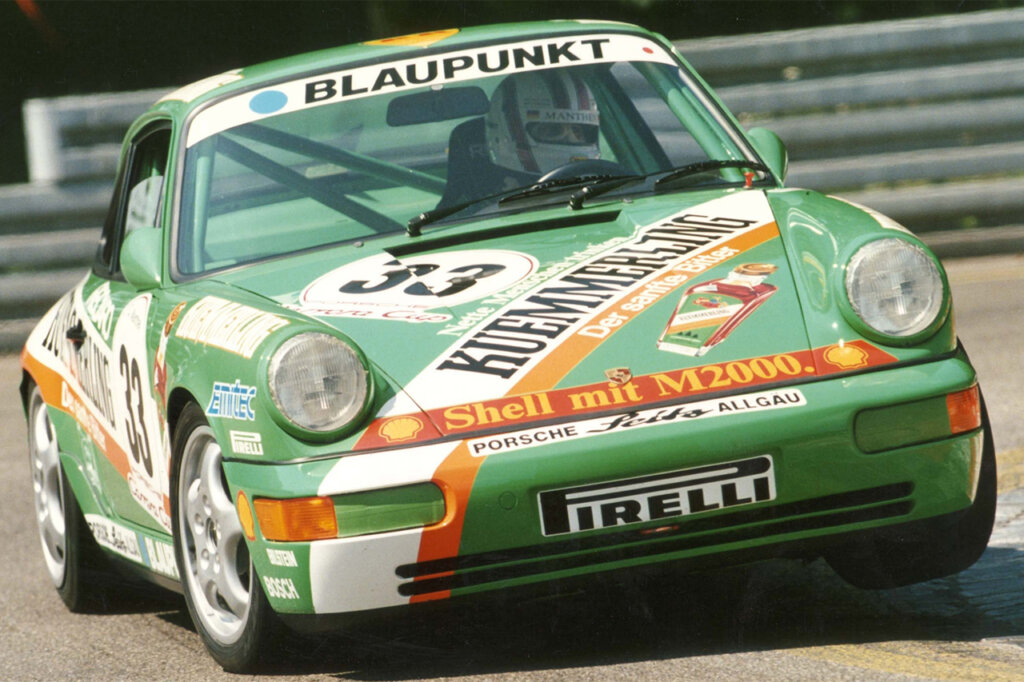 Green Porsche 964 going through a turn fast on the race track with a man wearing a white helmet