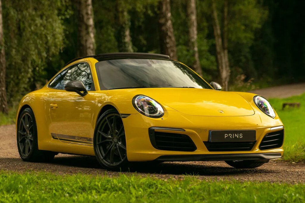 Yellow and black Porsche 911 Carrera T parked on a dirt road with trees in the background