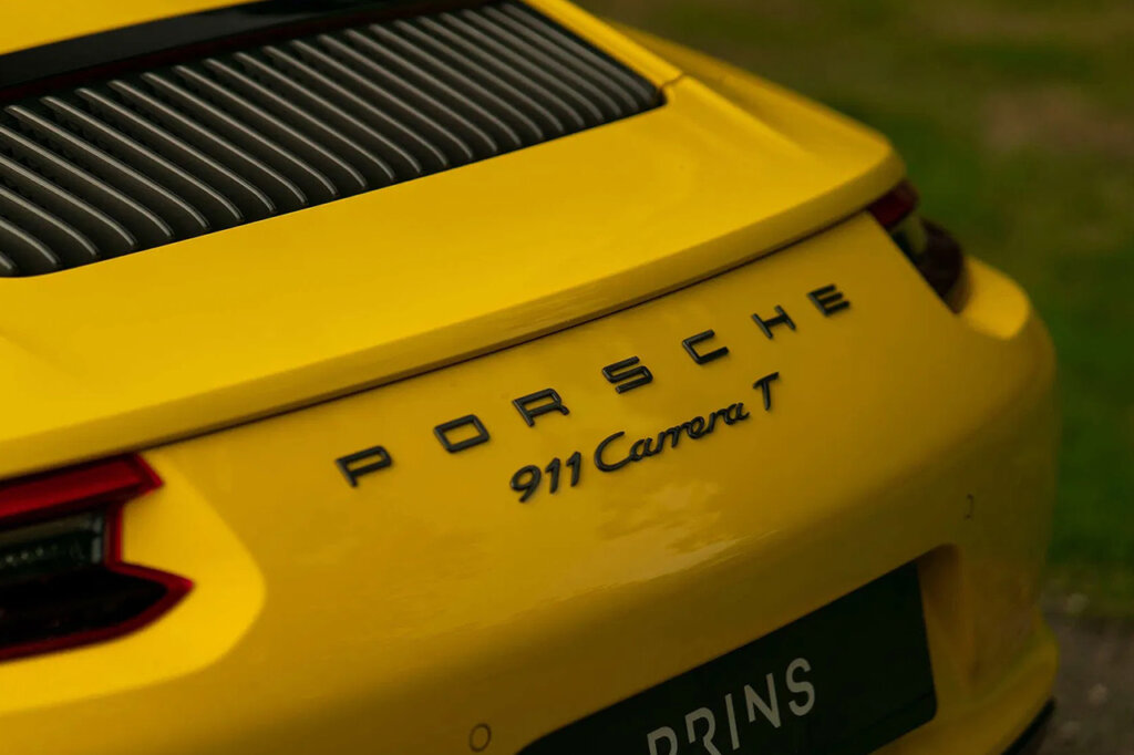 Yellow Porsche 911 Carrera T badging on the rear end of a yellow Porsche car with grass in background