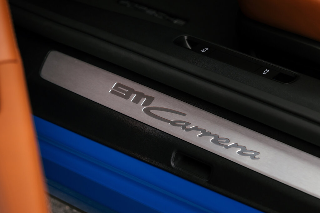 Door jam card that has a stamped 911 Carrera branding of a blue Porsche with an orange leather door peaking on the side