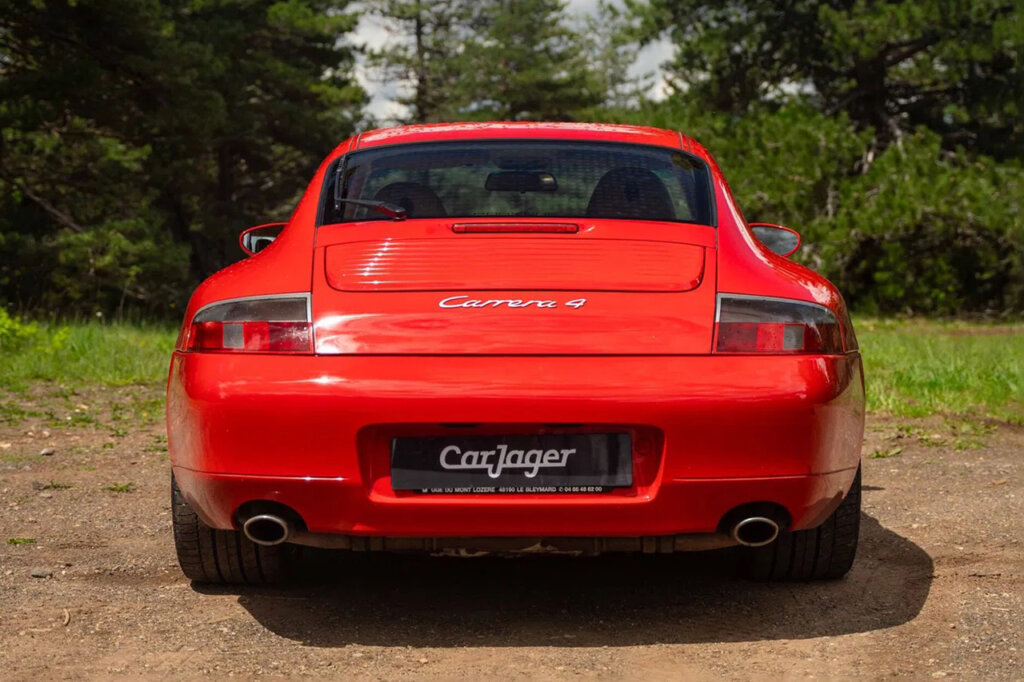 Red 911 carrera 4 parked on the ground near grass with trees in the background