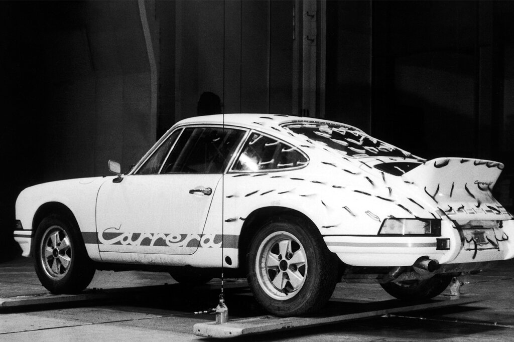 White and black photo of a White Porsche 911 carrera with tape along the backside of the car propped on two planks holding the car in the air