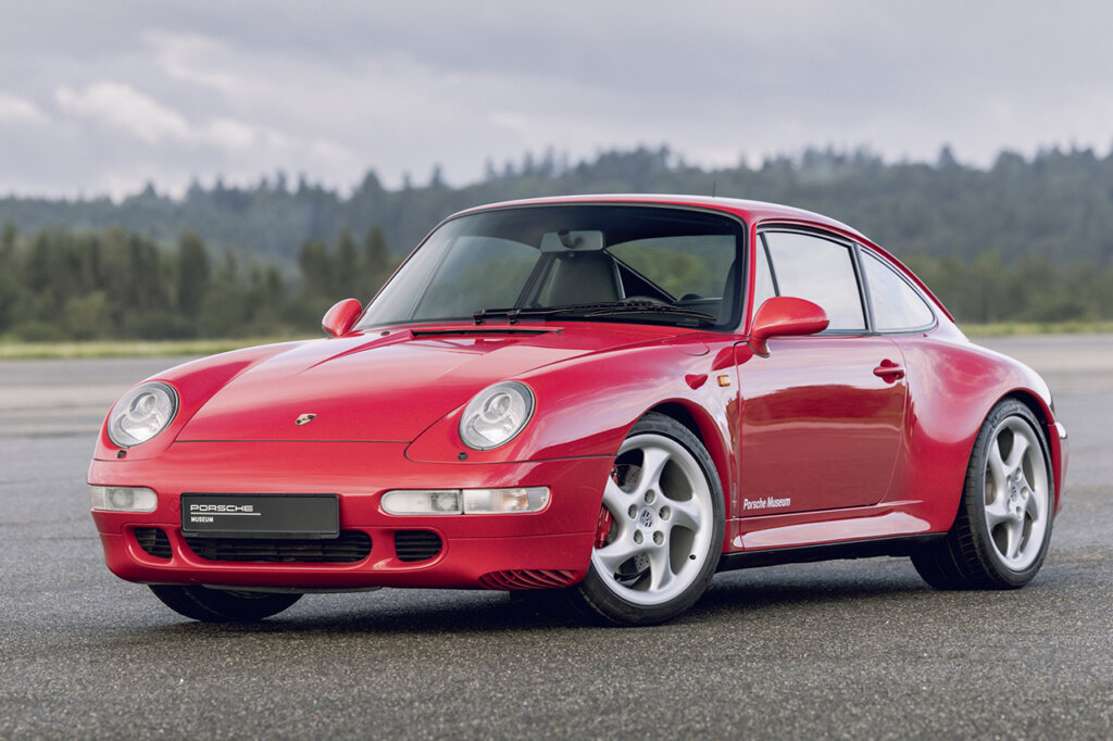 Pink 911 993 parked on asphalt with grey clouds and trees in the background