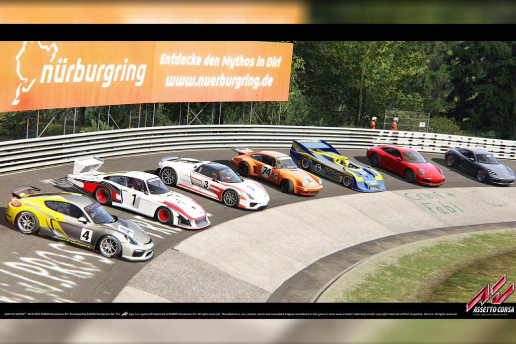 Row of Porsche cars in various colors and models along a curve of a race track with grass in front of the cars and an orange billboard poster behind them.