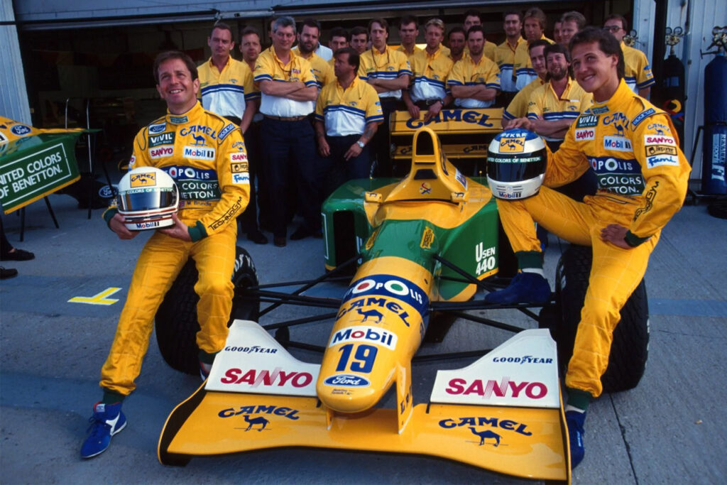 micheal schumacher, martin brundle, and the benetton team pose next to the Yellow and green benetton b192-05 f1 race car